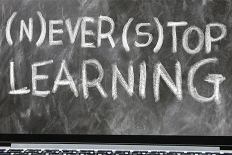 A laptop screen models a blackboard with the words "(N)EVER (S)TOP LEARNING".