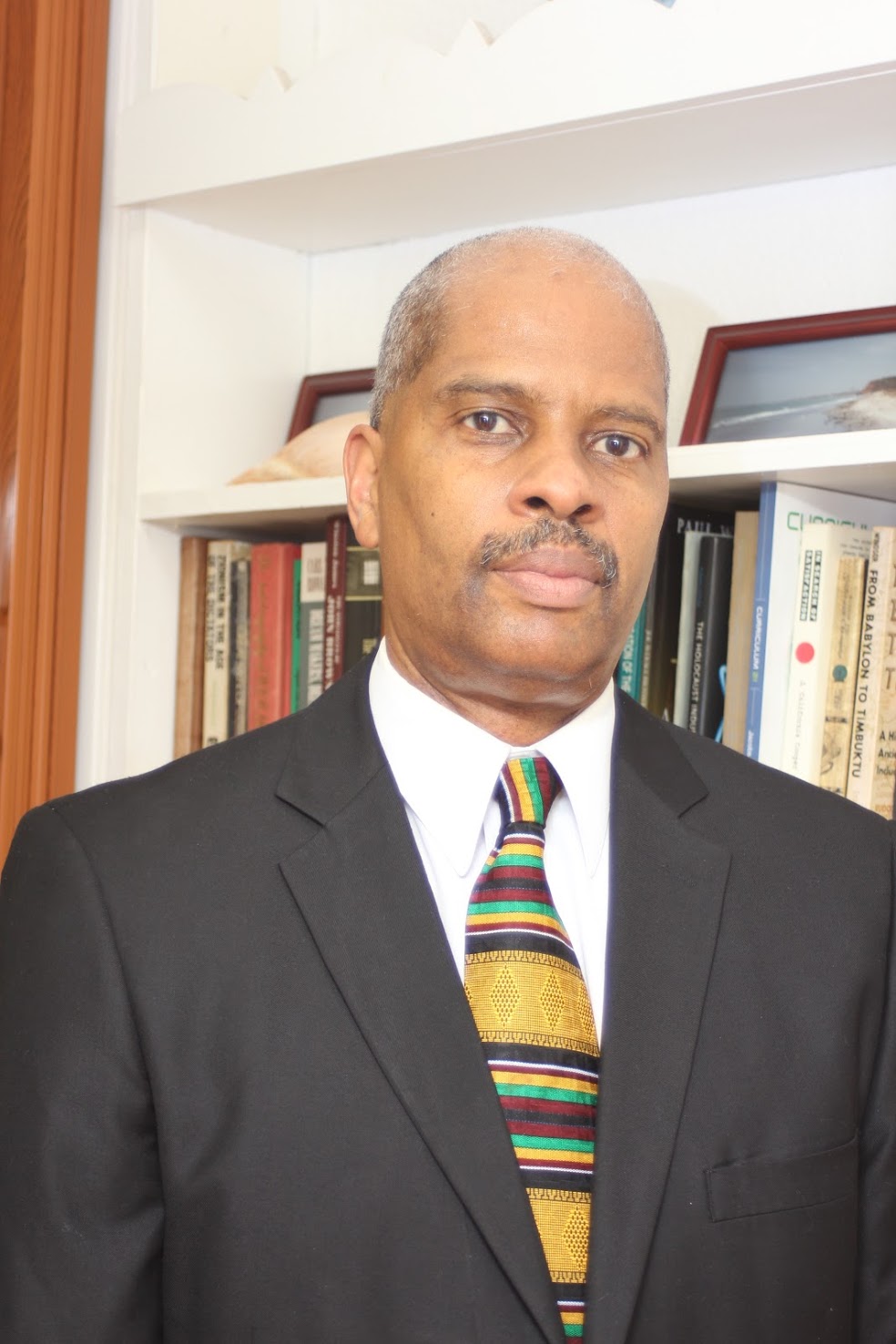 Photograph of Kyndall Brown wearing a tie next to a bookshelf
